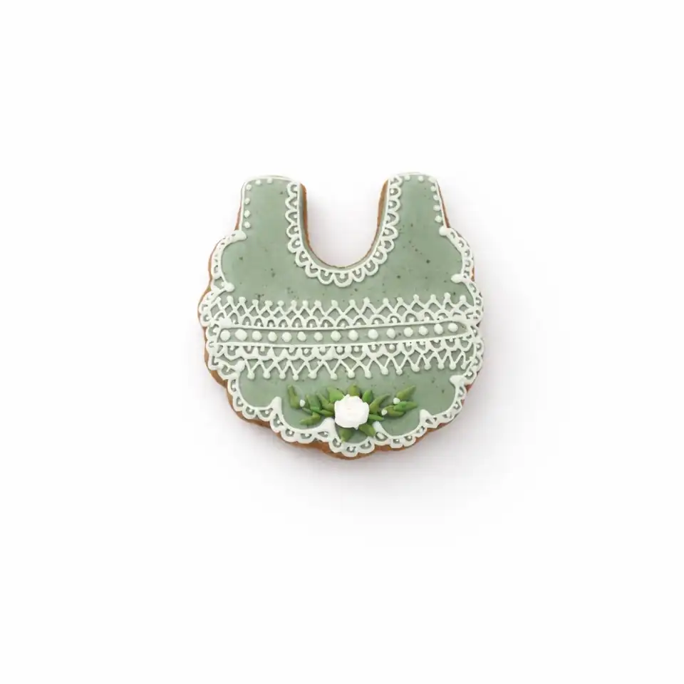 Bolacha de especiarias em formato de babador, decorada à mão com glacê real em verde sálvia e branco